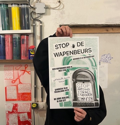 Iemand in een workshop houdt een poster omhoog met de tekst 'Stop de wapenbeurs'.
