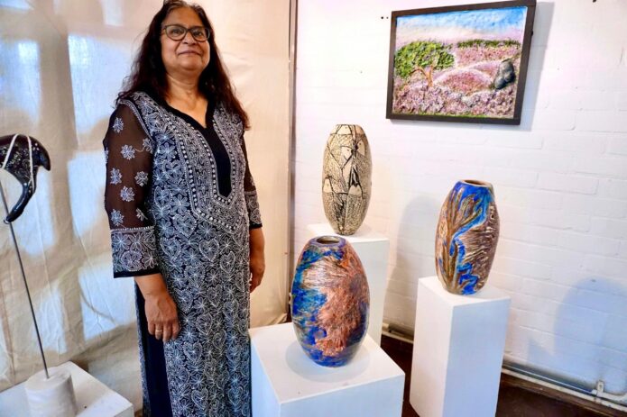 Portrait of Anita Kluge standing next to 3 of her vase sculptures.