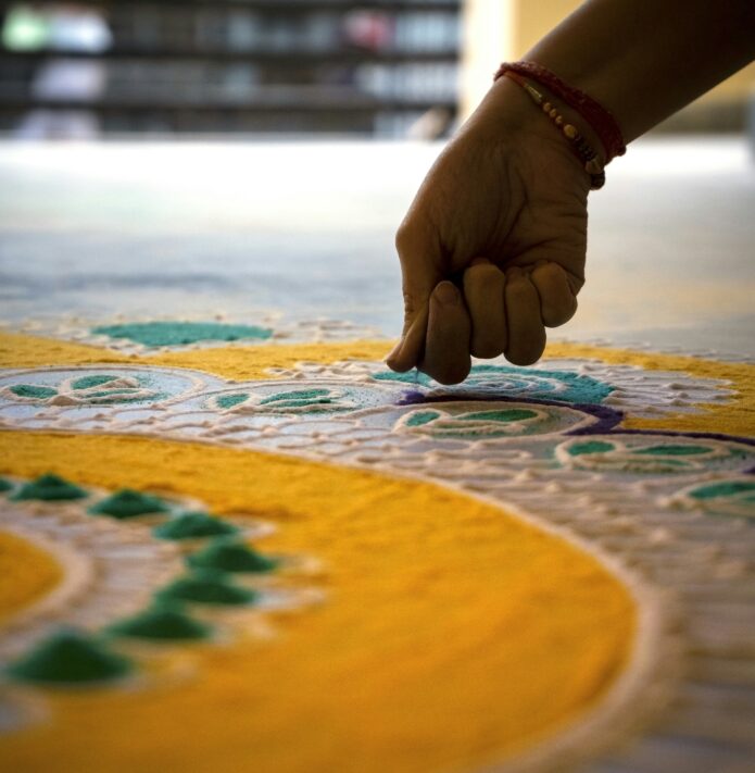 A photo of a someone's hand, spreading flour in a colourful and intricate pattern.