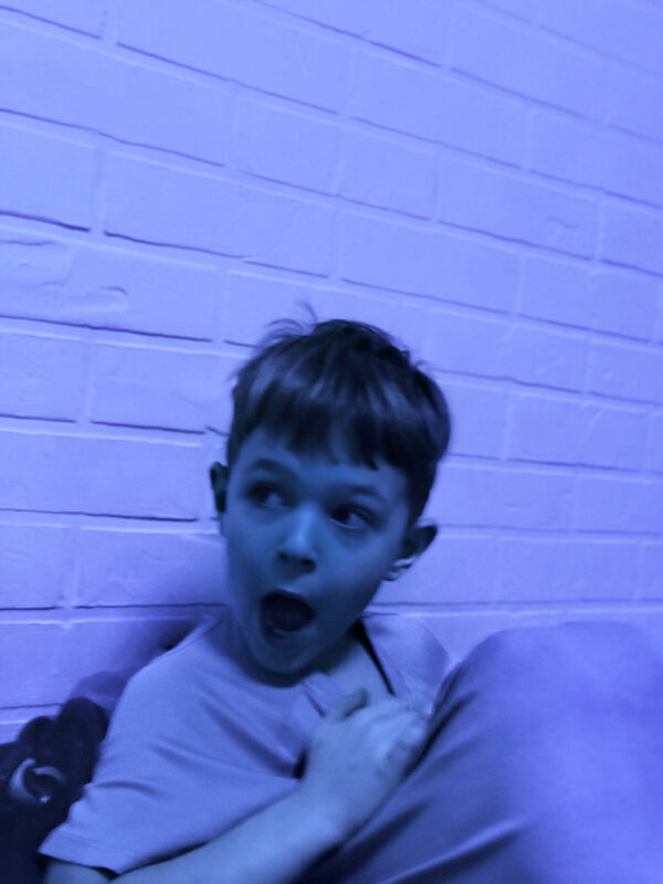 A young boy, shown in blue light, pulls an excited face.