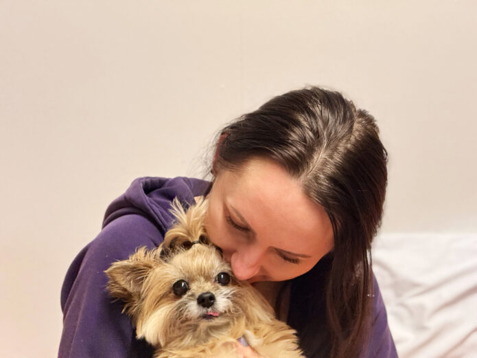 A woman cuddles a small, fluffy dog, her eyes looking down away from the camera.