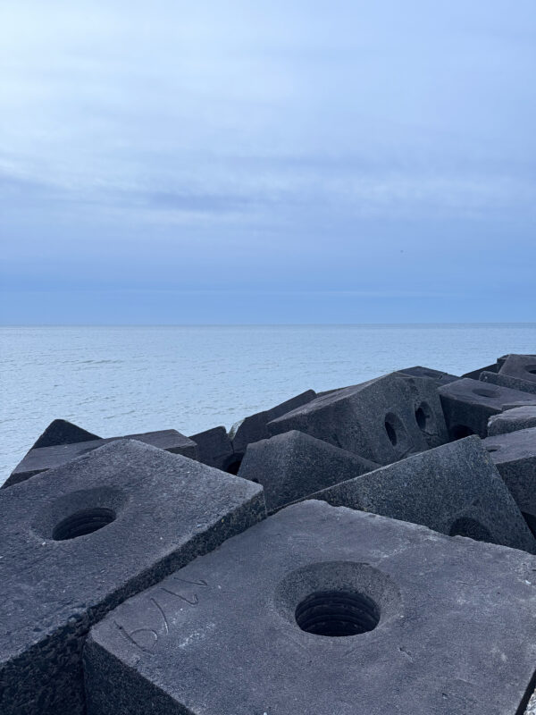 Dark concrete blocks on the beach in The Hague, with the calm blue sea in the background.
