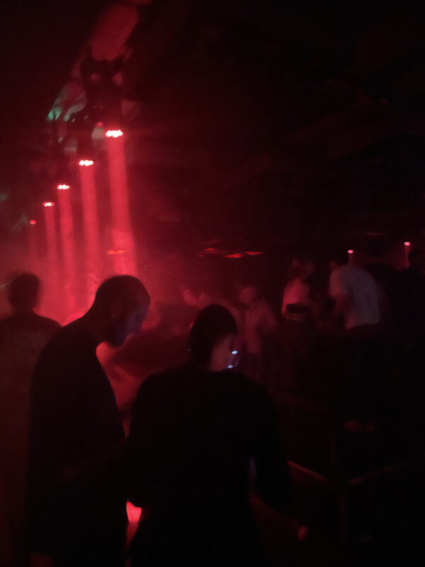 A man talking to a woman in a crowded nightclub illuminated by red spotlights.