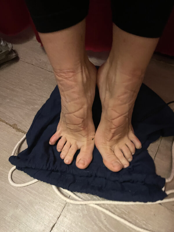 A pair of flexed, bare feet showing imprints of dance shoe laces.