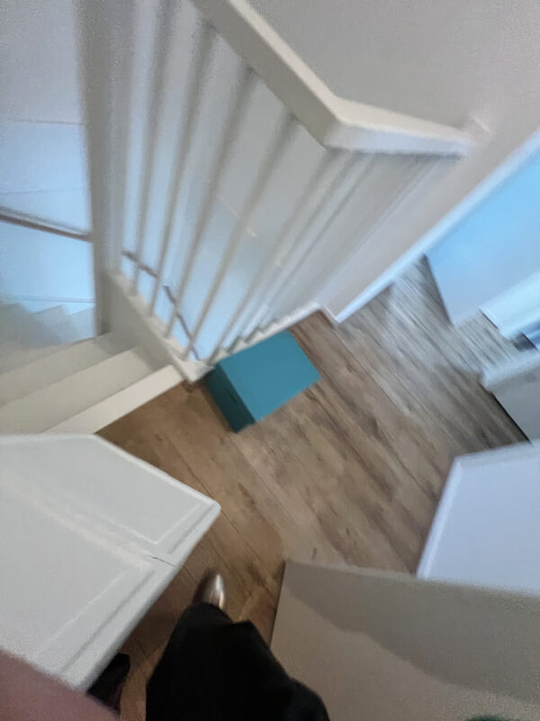 A slightly blurred photo of a wooden floor, a leg and shoe, and a steep winding staircase.